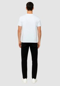 T-shirt bianca in cotone con scollo a girocollo, abbinata a pantaloni neri slim-fit e scarpe da ginnastica bianche, vista da dietro.