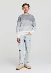 Szary i biały sweter w paski z okrągłym dekoltem, połączony z jasnoniebieskimi podartymi dżinsami i beżowymi sneakersami. Miękka, teksturowana tkanina.
