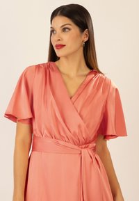 Korallenfarbnes Wickelkleid aus Satin mit kurzen, fließenden Ärmeln, tiefem V-Ausschnitt und gebundenem Taillendetail. Sanfte Textur und eleganter Fall.