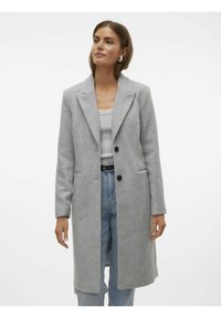 Cappotto grigio a spina di pesce con revers a punta, due bottoni neri e tasche laterali, abbinato a un top grigio e jeans in denim blu.