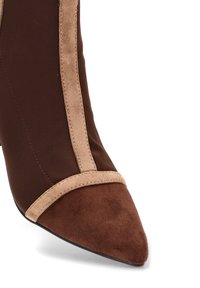 Botín marrón hasta el tobillo con puntera puntiaguda, que presenta una combinación de texturas lisas y de ante, y una banda de ante beige a lo largo de la costura.