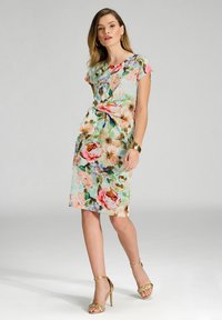 Robes florales à manches courtes en turquoise clair, ornées de grandes fleurs roses et dorées, avec une coupe ajustée et une longueur jusqu'au genou. Sandales à talons dorés.