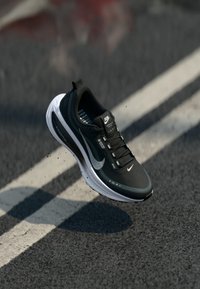 Zwart-witte Nike hardloopschoen in de lucht boven een asfaltweg met een witte streep, met zicht op de Gore-Tex branding en details van de ZoomX zool.