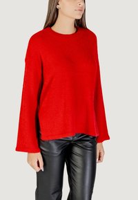 Maglione rosso, peloso, a maglia con scollo rotondo e maniche ampie, abbinato a pantaloni in pelle nera lucida. Design semplice e rilassato.
