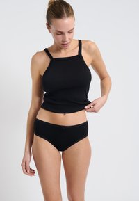 Canotta nera a coste con spalline sottili, abbinata a un'intimo a slip nero con un sottile dettaglio a fiocco. Texture liscia e design aderente.