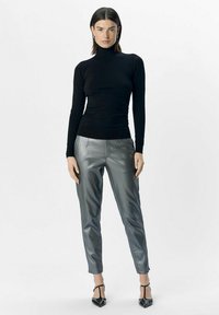 Zwarte langemouwen coltrui, gecombineerd met metallic zilveren tapered broek en zwarte hoge hakken. Soepele textuur en getailleerd ontwerp.