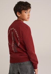 Mörkröd sweatshirt med långa ärmar, rund hals, med vit och grå textdesign på ryggen. Tyget ser slätt ut, avslappnad passform.