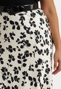 Svart blommönstrad kjol med en krämfärgad bakgrund, med en slät textur och ett glansigt svart bälte i midjan.