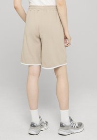 Beige woven shorts with an elastic waistband and white trim. Worn with gray athletic shoes and white ankle socks, shown from the back.