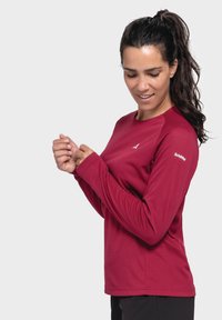 Langärmliges Active-Shirt in dunklem Rot, aus strukturiertem Material mit rundem Hals. Das Shirt verfügt über ein Logo auf der Brust und kontrastfarbige Schulterpaneele.