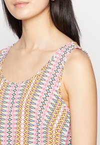 Top sin mangas con escote redondo, que presenta un patrón de zigzag colorido en rosa, azul, marrón y amarillo. Textura de tela suave.