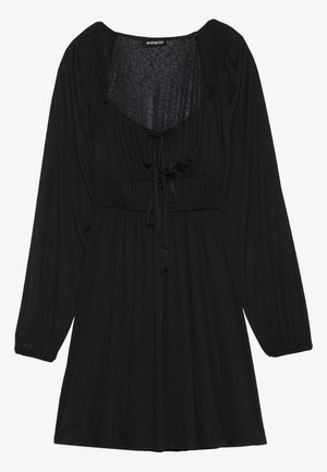 Svart kjole med lange ermer, scoop-neck og snøring i midjen. Laget av et strukturert stoff med rynkede detaljer på skuldrene.
