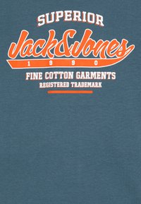 Mėlynas medvilninis marškinėliai su oranžiniu ir baltu "Jack & Jones" logotipu, taip pat užrašu "SUPERIOR" ir "FINE COTTON GARMENTS". Minkšta tekstūra.