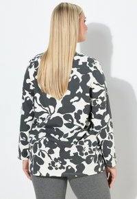 Langärmliges Hemd mit schwarzem und weißem Blumenmuster; legerer Schnitt; weicher Stoff; gerader Saum; kombiniert mit grauen Leggings.