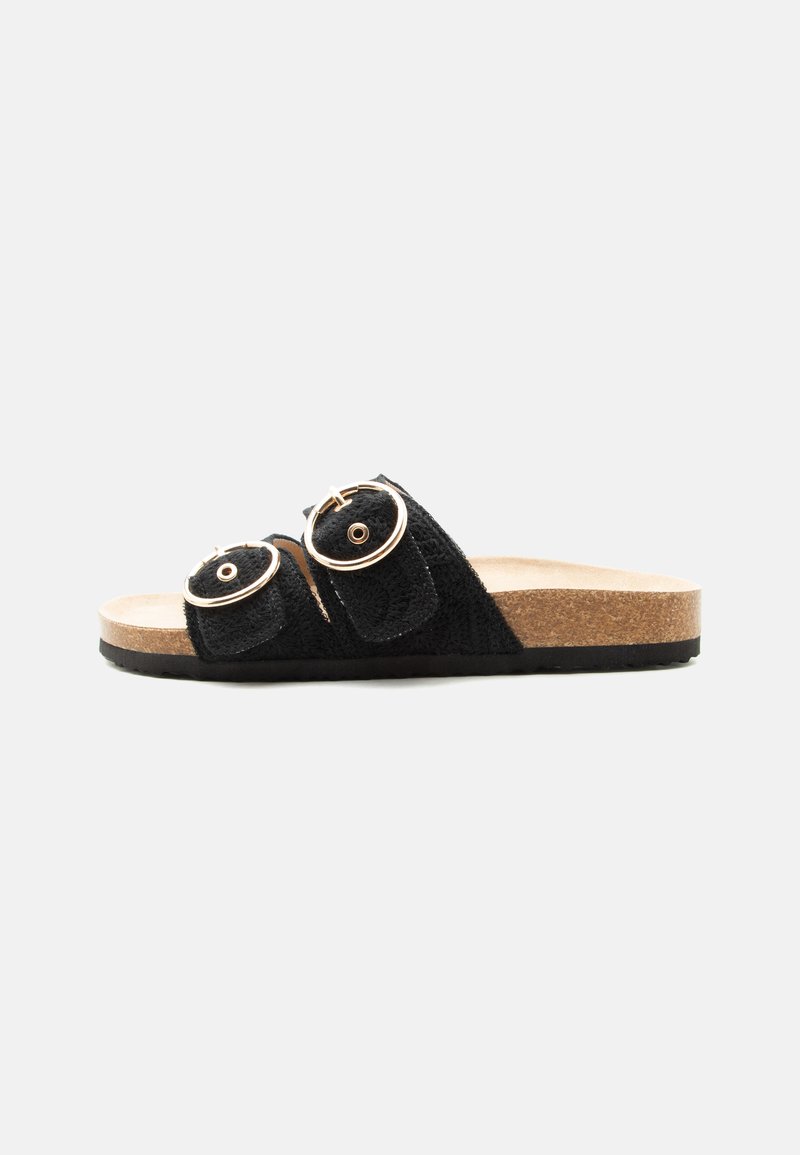 Sandale noire slip-on avec deux brides réglables à boucle et une semelle à lit de pied en liège sur un fond clair uni.