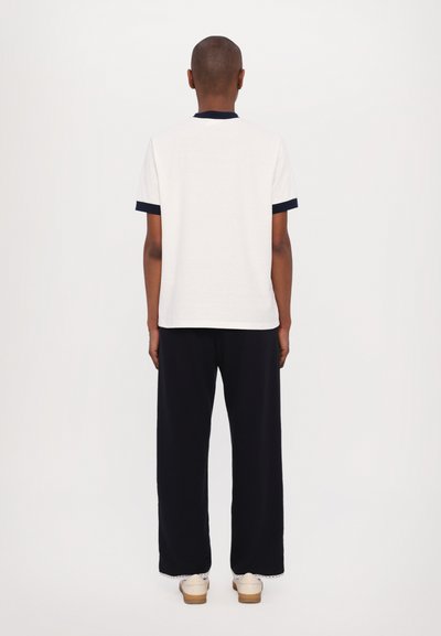 White t-shirt with navy collar and cuffs, paired with black wide-leg trousers. The fabric appears soft with a smooth texture.