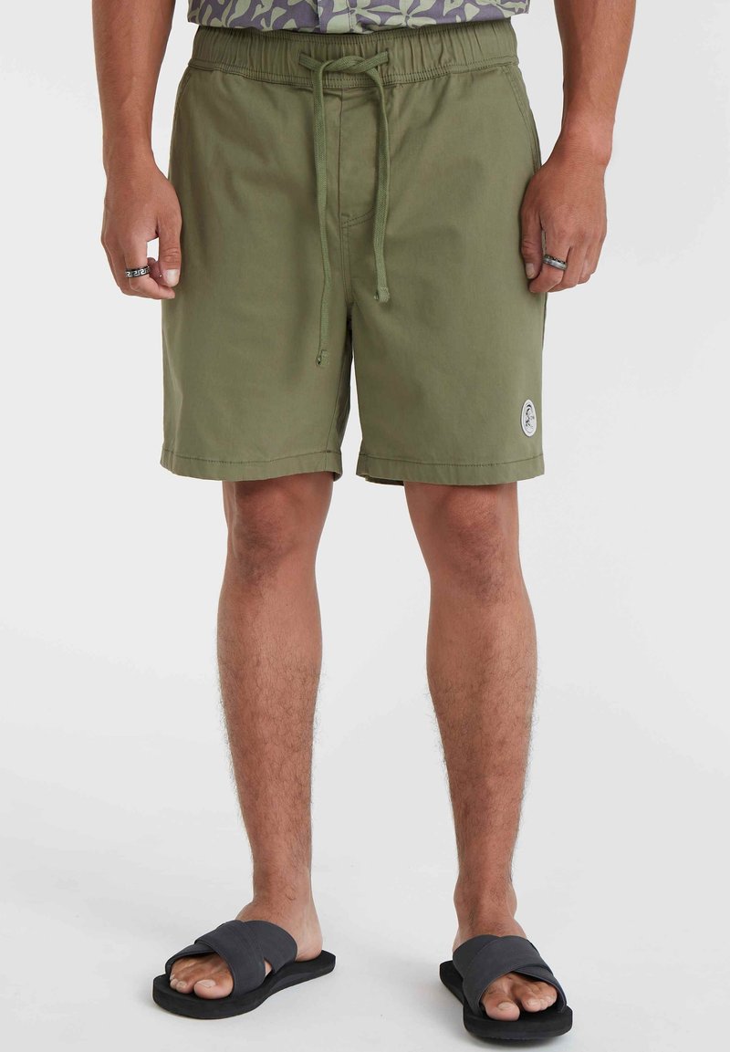 Olivgrüne Badeshorts mit elastischem Bund und Kordelzug. Mit einem kleinen Logopatch am linken Bein. Kombiniert mit schwarzen Flip-Flops.