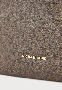Tissu marron texturé présentant un motif géométrique, avec un logo "Michael Kors" doré bien en vue.