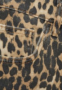 Denim w panterkę z mieszanką czarnych plam na beżowym tle, z widocznym przeszyciem i małą kieszonką.