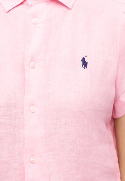 Cămașă scurtă cu mâneci roz deschis, cu nasturi, având un logo mic brodat cu un jucător de polo în albastru închis pe pieptul stâng.