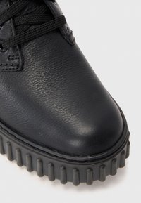 Chaussure en cuir noir avec un dessus texturé, bout rond et épaisse semelle en caoutchouc striée. Présente des lacets noirs et des détails de couture.