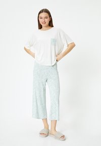 T-shirt blanc à manches courtes avec une poche en vert menthe à motifs, associé à un pantalon cropped vert menthe orné d'un motif paisley et des chaussons en gris peluche.
