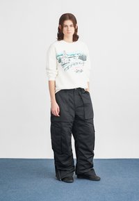 Witte sweatshirt met kleurrijke winterlandschapprint, gecombineerd met losse zwarte cargobroeken. Soepele textuur, rechte silhouet, met ritssluiting aan de onderkant.