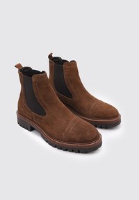 Braune Wildleder Chelsea-Boots mit elastischen Seitenpaneelen, einer abgerundeten Spitze und einer strukturierten Gummisohle mit einem kontrastierenden braunen Rand.