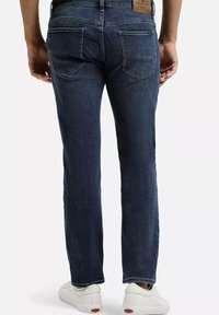 Ciemnoniebieskie dżinsy o prostym kroju, z dwiema tylnymi kieszeniami i skórzaną metką na talii. Noszone z białymi sneakersami.