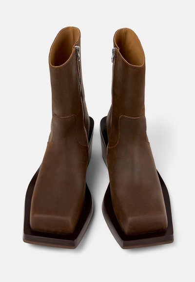 Bottines en cuir marron avec un embout carré, dotées d'une fermeture éclair sur le côté et d'une semelle épaisse marron. Texture lisse avec un minimum de détails.
