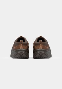 Las zapatillas deportivas marrones cuentan con un material texturizado y un cuello acolchado, una suela oscura y una etiqueta en el talón para facilitar el uso.
