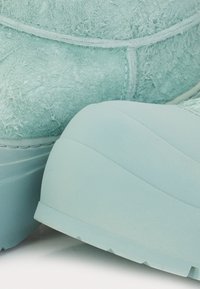 Detailní záběr na světle modré semišové boty s tlustými, strukturovanými gumovými podrážkami a viditelným šitím na svrchním materiálu.