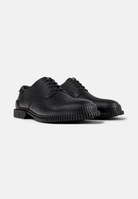 Scarpe in pelle nera con lacci, suole testurizzate e robuste e punte arrotondate su uno sfondo neutro.