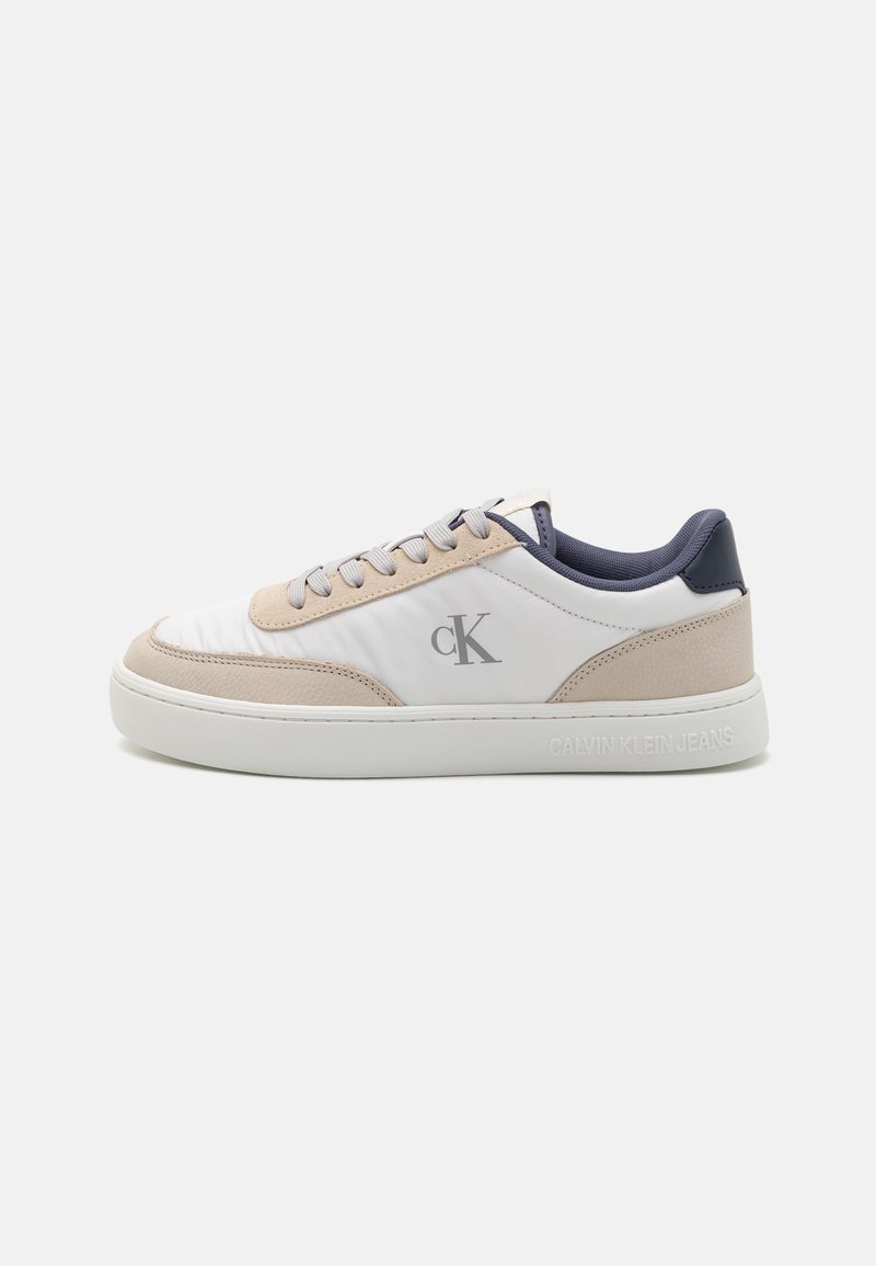 White and beige sneaker with a textured upper, featuring navy accents, round laces, and a logo on the side. Rubber sole for grip.