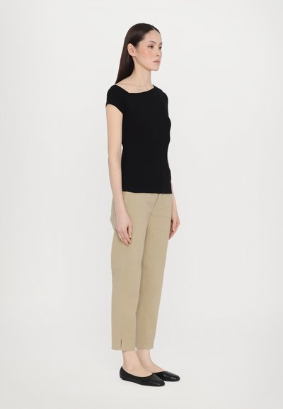 Top negru ajustat cu mânecă scurtă, asortat cu pantaloni tapered bej deschis, cu fante laterale, purtat cu pantofi negri fără toc.