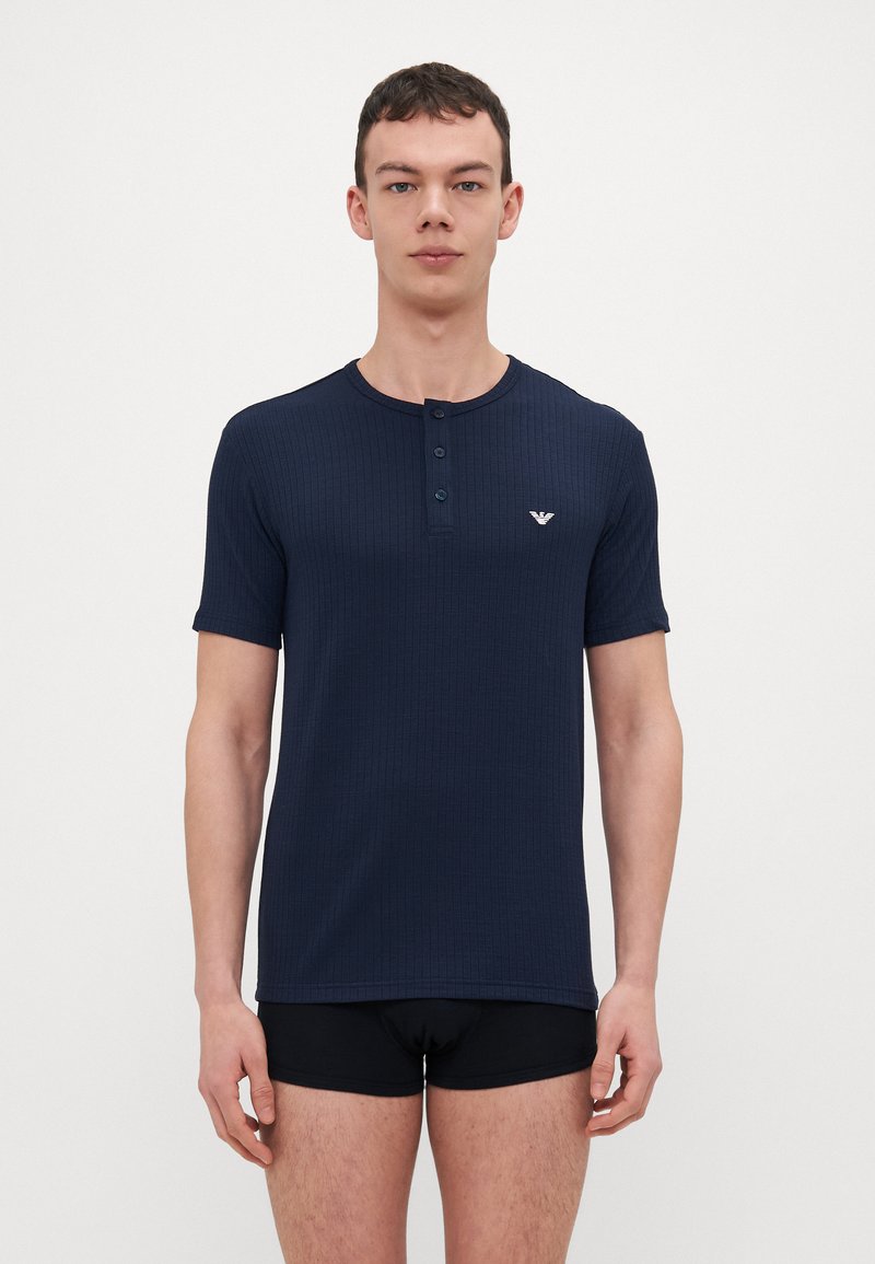 T-shirt henley à manches courtes côtelé marine avec trois boutons, arborant un petit logo sur la poitrine gauche, fabriqué en tissu doux pour le confort.