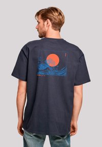 Navyblauwe katoenen t-shirt met op de achterkant een grote graphic van een rode zon en blauwe golven, met verticale tekst en een rechthoekige omlijning.