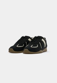 Pair of black leather sneakers with beige stripes and gum rubber soles on a white background, viewed from front-left angle.
