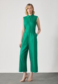 Green sleeveless jumpsuit with a collar, front buttons, a belt at the waist, and wide cropped legs; smooth fabric with a matte finish.