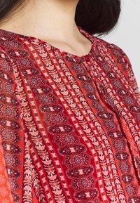 Tissu à motif floral rouge avec des rayures verticales, présentant un col boutonné et une texture douce. Léger et tombe avec fluidit é.