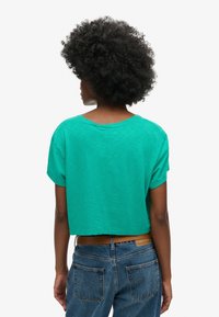 Kortærmet, crop top i kraftig grøn bomuld. Har en rund halsudskæring og en afslappet pasform, parret med højtaljede blå jeans.