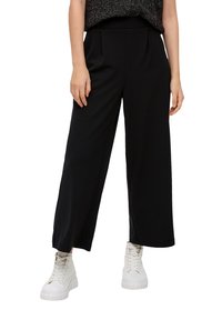 Pantaloni neri a gamba larga in materiale morbido con vita alta e pieghe frontali, abbinati a sneaker bianche con lacci.