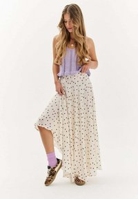 Žena s dlhými vlnitými vlasmi v fialovom bezrukávovom pulóvri, bielych sukňach s bodkami, fialových ponožkách a teniskách s leopardím vzorom.