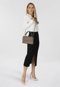 Borsa a tracolla marrone con motivo, indossata a spalla, abbinata a una camicia bianca e a una gonna nera al ginocchio con uno spacco laterale.