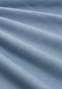 Lichtblauwe stof met zachte plooien en een gladde, licht gestructureerde oppervlakte, getoond in close-up.