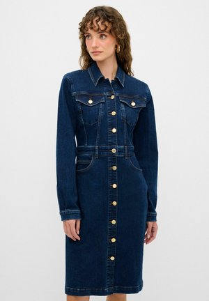Robe en denim bleu foncé avec des manches longues, fermeture avant boutonnée, deux poches poitrine et une taille cintrée. Présente des boutons dorés et des coutures discrètes.