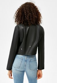 Korte zwarte leren jas met een gladde structuur, voorzien van gestructureerde schouders, zichtbare naden en drukknopen, gecombineerd met lichte denim jeans.