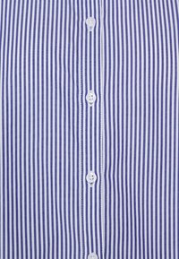 Chemise à manches longues avec des rayures verticales violettes et blanches. Fabriquée en tissu lisse, elle dispose d'un col classique et de boutons blancs.