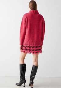 Červený pletený svetr s vysokým, pleteným límcem, doplněný o mini sukni s třásněmi v růžové a černé barvě. Černé lesklé kozačky na podpatku nad kolena.
