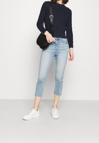 Suéter de punto navy, vaqueros cortos de color azul claro con dobladillo deshilachado y zapatillas blancas. Bolso negro de hombro con forma redonda.